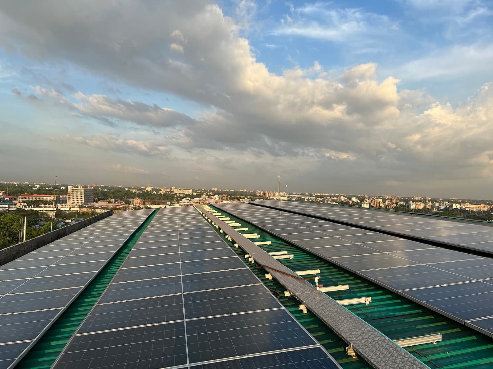 Rows of rooftop solar panels stretching toward the Dhaka skyline under a bright sky