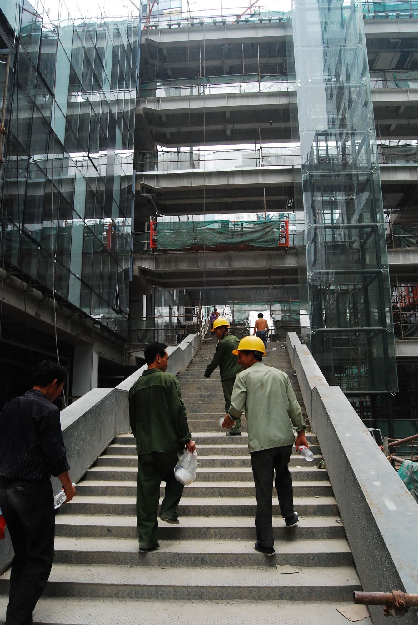 中国,戴着安全帽的建筑工人在一座在建玻璃塔内攀爬混凝土楼梯。