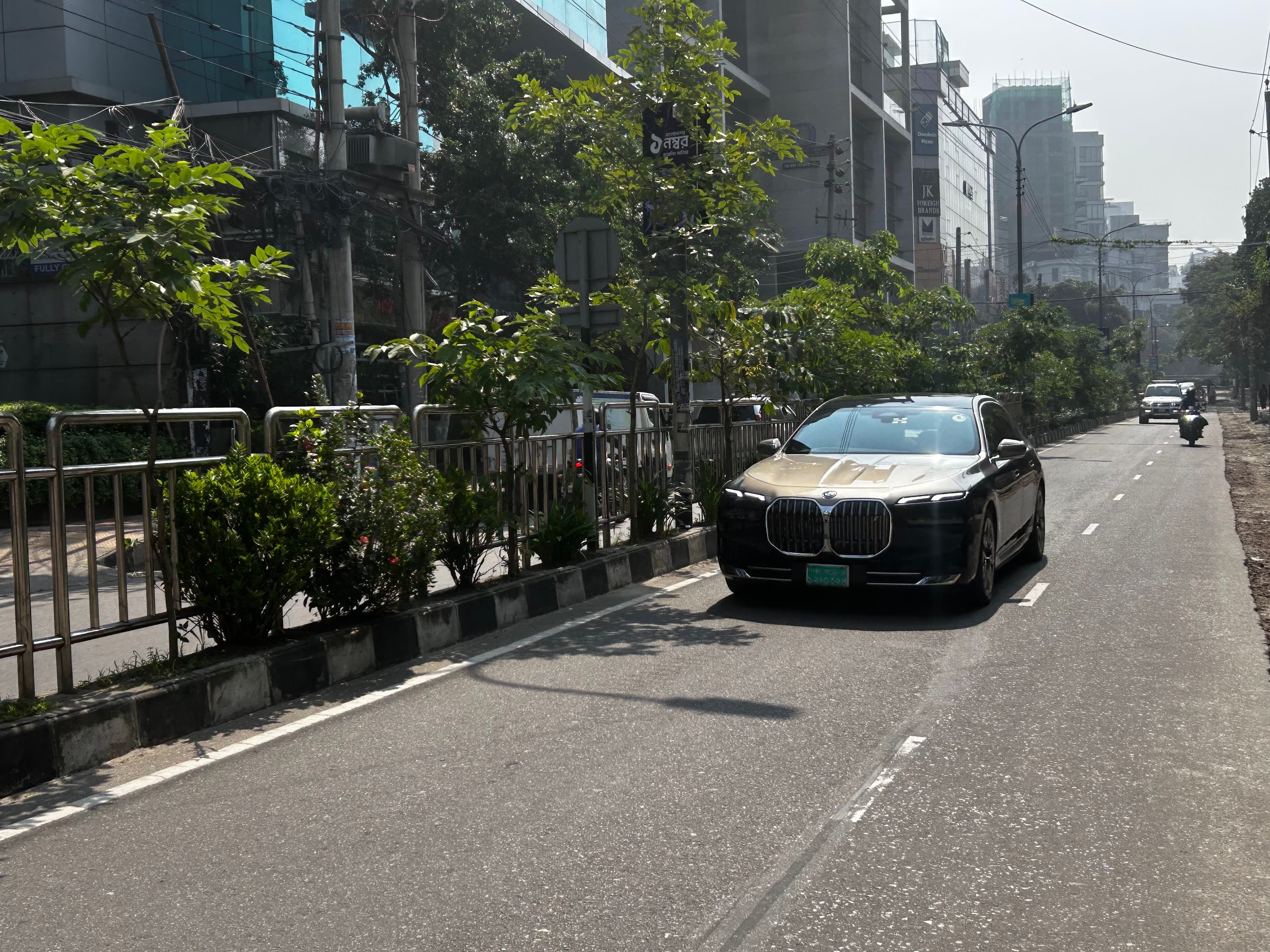 2026年,一辆黑色电动宝马7系轿车行驶在达卡一条绿树成荫的大道上。